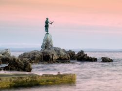 La ragazza col gabbiano, statua simbolo di Opatija, si staglia contro il rosa del tramonto a due passi dal lungomare cittadino, con lo sguardo verso il mare Adriatico - © Sinisa Botas / ...
