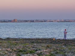 Pescatore sullo Jonio in Puglia,  sullo sfondo Porto Cesareo al tramonto con visibile Torre Chianca