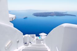 Una scala bianca di un villaggio di Santorini, con sullo sfondo i vulcani  Nea e Paleo Kameni, ed una nave da crociera - © freedombreeze / Shutterstock.com