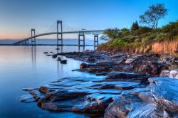 Alba sul ponte di Newport, Rhode Island, USA. Una suggestiva veduta dal Taylor's Point nei pressi di Jamestown con i paesaggio roccioso in primo piano.

