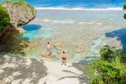 Alofi, isola di Niue: un uomo e una donna in costume da bagno sulla barriera corallina di fronte alla spiaggia isolata immersa nella vegetazione - © Brian S / Shutterstock.com
