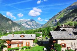 Alpi in estate, Valle d'Aosta, Italia. Cielo azzurro con qualche nuvola e vegetazione verde brillante fanno da cornice alle Alpi.



