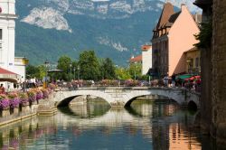 Antichi palazzi affacciati su un canale di Annecy, Francia. Sullo sfondo le cime delle montagne che fanno da cornice alle acque blu scuro.

