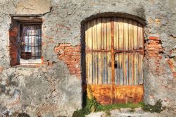 Un vecchio muro di mattoni con un cancello di ferro e una piccola finestra caratterizzano la facciata di questo antico casale di La Morra, Cuneo, Pimeonte
