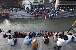 Cerimonia di cremazione lungo il fiume Bagmati a Kathmandu, Nepal. Fedeli durante la cerimonia funebre che si svolge quotidianamente con i corpi dei morti cremati sulle pire prima della dispersione ...