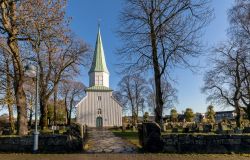 Chiesa bianca in legno con campanile a Kristiansand, Norvegia. A questo grazioso edificio religioso si accede tramite un vialetto in pietra affiancato dal cimitero.

