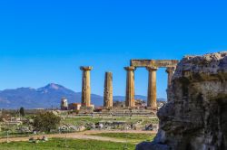 Colonne al Tempio di Apollo nell'antica Corinto, Grecia. Sullo sfondo, una chiesa e la sagoma delle montagne.

