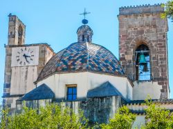 Dettagli della chiesa dell'Immacolata Concezione nel centro di Barumini, Sardegna: una torre campanaria con l'orologio, la cupola colorata e il campanile. Le forme tardogotiche sono ...