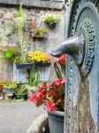 Dettaglio della fontana nel centro di Saint-Bertrand-de-Comminges (Francia). Sullo sfondo, fiori colorati decorano la facciata di una vecchia casa.



