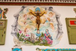 Un dipinto religioso con croce in legno sulla facciata di una casa a Canazei, Val di Fassa, Trentino Alto Adige.
