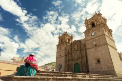 Una donna con la tradizionale keperina sulla schiena sui gradini della cattedrale di Puno, Perù.

