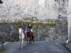 Due donne a cavallo in un vicolo di Saint-Bertrand-de-Comminges (Francia). Sullo sfondo, il muro della cattedrale, ex convento del XIX° secolo - © Dan Shachar / Shutterstock.com