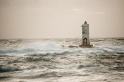 Faro di Mangiabarche a Calasetta con il mare in burrasca (Sardegna). Su un piccolo scoglio che sorge davanti alla spiaggia di Mangiabarche s'innalza un faro solitario che ha il compito di ...