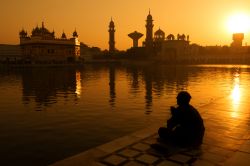 Fedeli sikh seduti al tramonto lungo la piscina sacra del Tempio d'oro a Amritsar, Punjab, India.

