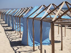 Una fila di casette con teli bianchi e blu sulla spiaggia di Costa da Caparica, Portogallo.

