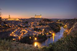 Un romantico panorama di Toledo al crepuscolo, con le luci cittadine che si riflettono sulla superficie del Tago e la sagoma illuminata del Castello dell'Alcazar sullo sfondo  - © ...