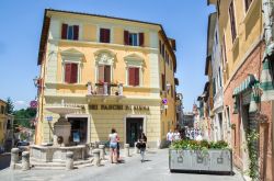 Gente a passeggio nella piccola piazza con la fontana a Asciano, provincia di Siena, Toscana - © Luca Lorenzelli / Shutterstock.com