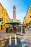 Gente ai tavolini di un bar nel centro di Nimes, Francia. Sullo sfondo, la torre dell'orologio - © trabantos / Shutterstock.com