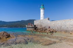 Gente al mare nei pressi della spiaggia di Propriano, Corsica. Sullo sfondo, il faro della città che si affaccia sul Golfo di Valico - © Eugene Sergeev / Shutterstock.com 