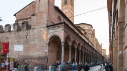 Gente cammina lungo la medievale Cerchia dei Torresotti a Bologna, Emilia-Romagna. Una bella veduta della chiesa di San Giacomo Maggiore da Via Zamboni - © vvoe / Shutterstock.com