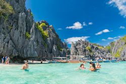 Gente in relax nelle acque tropicali di Palawan, isola delle Filippine. Sullo sfondo, le tipiche barche in legno - © DiegoMariottini / Shutterstock.com