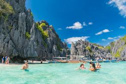 Gente in relax nelle acque tropicali di Palawan, isola delle Filippine. Sullo sfondo, le tipiche barche in legno - © DiegoMariottini / Shutterstock.com