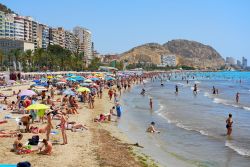 Gente in spiaggia sulla famosa Postiguet Beach a Alicante in estate, Spagna. Principale spiaggia della città, è caratterizzata da acque cristalline, sabbia dorata, palmeti e uno ...
