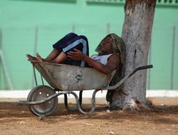 Un giovane ragazzo riposa seduto in una carriola a Luanda, Angola, all'ombra di un albero - © terezinhka / Shutterstock.com