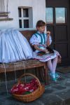 Holloko, Ungheria: una bambina con abiti tradizionali seduta su una panca davanti a una casa del villaggio - © Orsolya_ L / Shutterstock.com