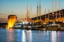 Il castello Kamerlengo affacciato sul porto di Trogir, Croazia, fotografato di sera. In primo piano, barche ormeggiate al porto.



