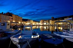 Il porto di Cres by night, isola di Cres, Croazia. I palazzi illuminati si rispecchiano nelle acque del mare creando un'atmosfera magica.


