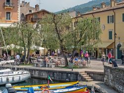 Il vecchio porto di Torri del Benaco, provincia di Verona. Sullo sfondo, uno scorcio del centro storico con edifici e turisti - © 167880122 / Shutterstock.com