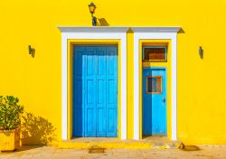 La colorata facciata di una casa sull'isola di Spetses, Grecia: due porte azzurre impreziosiscono il muro giallo acceso.


