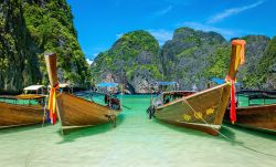 La famosa spiaggia di Maya Bay sull'isola di Phi Phi, Thailandia. In primo piano barche in legno e sullo sfondo colline calcaree con vegetazione. Sabbia bianca, acqua limpida e rocce che ...