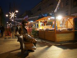 La statua di Julian Tuwim e la fiera di Natale a Lodz, Polonia. Il monumento "La panchina di Tuwim" con le bancarelle natalizie illuminate in occasione delle festività in Piotrkowska ...