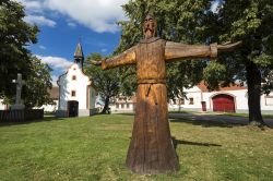 La statua in legno nella piazza centrale di Holasovice, Repubblica Ceca. Sullo sfondo la cappella e le abitazioni del paese - © Fulcanelli / Shutterstock.com