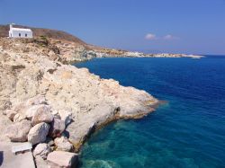 L'acqua blu del Mare Egeo lambisce la costa rocciosa dell'isoletta di Kimolos, Grecia.

