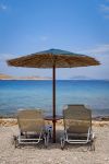 Lettini e ombrellone in paglia su una tranquilla spiaggia di Chalki, Dodecaneso, Grecia.

