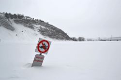 Il fiume Montmorency ghiacciato e coperto di neve in Quebec. Il cartello avverte della pericolosità del nuoto nelle acque del fiume Montmorency. In inverno le sue acque sono completamente ...