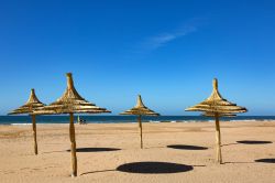 Ombrelloni in paglia sulla spiaggia lambita dalle acque dell'oceano Atlantico, nei pressi di Taghazout, Marocco.



