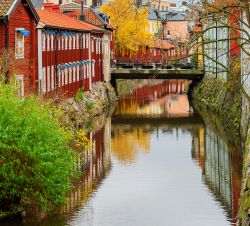 Paesaggio naturale con le tipiche case in legno e un ponte sullo sfondo, Vasteras, Svezia. I colori dell'autunno si riflettono nelle acque di questo canale.


