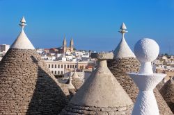 Panorama sui tetti dei trulli di Alberobello, Puglia, in una giornata di sole. Sullo sfondo, la skyline della cattedrale cittadina.

