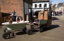 Partecipanti all'annuale Hat Fair impegnati in un giro della città in un bagno mobile a Winchester, Inghilterra. Indossano costumi e sono immersi nell'acqua calda - © Peter ...