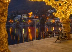 Particolare della passeggiata lungolago a Ascona, Svizzera. Le luci delle abitazioni e delle decorazioni luminose si riflettono sulle acque del Lago Maggiore - © RnDmS / Shutterstock.com ...