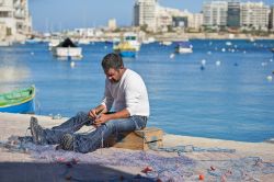 Un pescatore mentre rammenda le sue reti. La scena è stata ripresa sull'Isola di Malta, a nord-est de La Valletta, più precisamente sulla marina di St Julian's - © ...