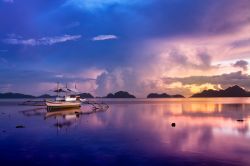 Un pittoresco tramonto sulla baia di El Nido, isola di Palawan, Filippine. In primo piano, una tradizionale barca in legno.
