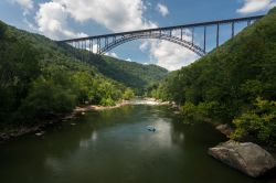 L'alto ponte ad arco nelle gole del New River, West Virginia. Un gommone con turisti si dirige verso le rapide del fiume.

