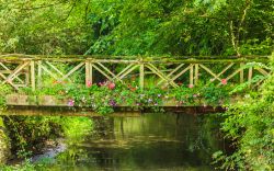Un ponticello sul fiume Coln a Bibury, Inghilterra - Un ponte pedonale in legno impreziosito da vegetazione e fiori variopinti: gli scorci panoramici offerti dal fiume Coln sono fra i più ...