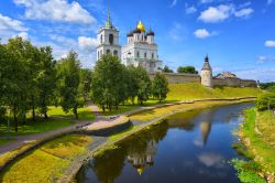 Pskov, Russia: la torre di avvistamento, le mura e la cupola d'oro della cattedrale della Trinità con i riflessi sull'acqua del fiume Velikaja.



