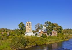 Regione di Pskov: un'antica chiesa ortodossa, in pietra e calce, con il campanile sulle sponde del fiume, Russia.
